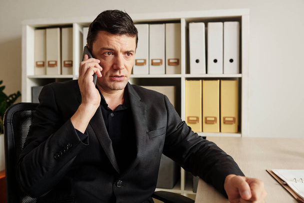 Portrait d'un homme d'affaires en colère parlant au téléphone avec un collègue et frappant la table avec un poing serré - Photo, image