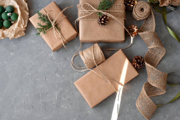 Βιώσιμη Χριστουγεννιάτικη γιορτή, προετοιμασία δώρων. Σπιτική συσκευασία δώρου με craft καφέ χαρτί, διακόσμηση με κουκουνάρια, κλαδιά, κορδόνι γιούτας. Οικολογικό πακέτο δώρων. - Φωτογραφία, εικόνα