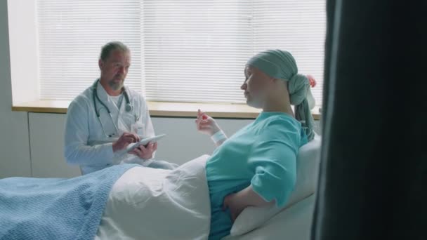 Μέτριο πλάνο της νεαρής γυναίκας με καρκίνο επικοινωνεί με το γιατρό, ενώ βρίσκεται στο κρεβάτι στο θάλαμο νοσοκομεία - Πλάνα, βίντεο