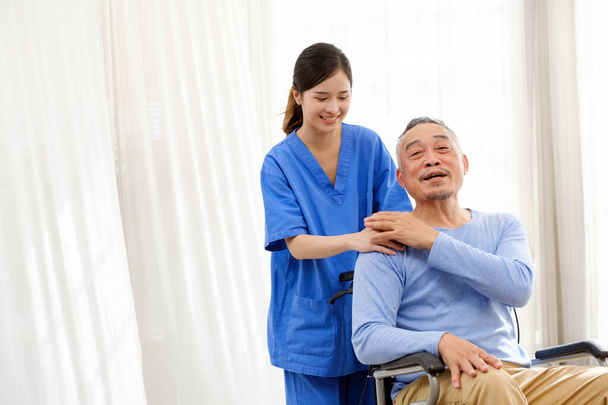 Opiekun terapeuta stoi z azjatyckim seniorem siedzącym na wózku inwalidzkim i dotyka ich rąk na starszym ramieniu razem. Dom opieki wspomaga grupę wsparcia. Obraz z przestrzenią do kopiowania - Zdjęcie, obraz