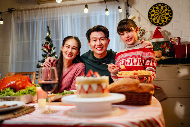 Happy and Cheerful group of extended Asian family and daughter smiling during Christmas dinner at home. Celebration holiday together. Family gatherings and reunions. Focus on young Asian family. - Photo, Image