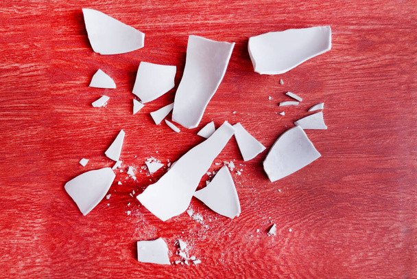Taustalla White Shards of a Broken Plate. pirstoutuneen lautasen sirpaleita. Lattialla on valkoisia astioita. Terät ja palaset rikkinäisestä astiasta. Yläkuva - Valokuva, kuva