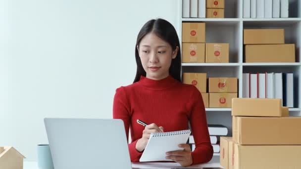 e-kereskedelem, kisvállalkozás, sme, gyönyörű ázsiai nő nézi a számítógépet, és használja jegyzet figyelembe vevői megrendelések és keres az online értékesítés mosolygós arc boldog munka közben. Kiváló minőségű 4k - Felvétel, videó