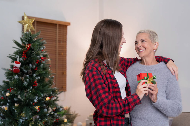 Κόρη δίνει δώρο στην ευτυχισμένη μητέρα και αγκαλιάζει τους εσωτερικούς χώρους στο σπίτι τα Χριστούγεννα. - Φωτογραφία, εικόνα