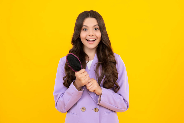 Teenager dívka kartáčování vlasy s hřebenem na žluté izolované pozadí studia. Kadeřník pro dospívající dívku s kartáčem na vlasy. Dětský účes. Šťastná tvář, pozitivní a usměvavé emoce dospívající dívky - Fotografie, Obrázek
