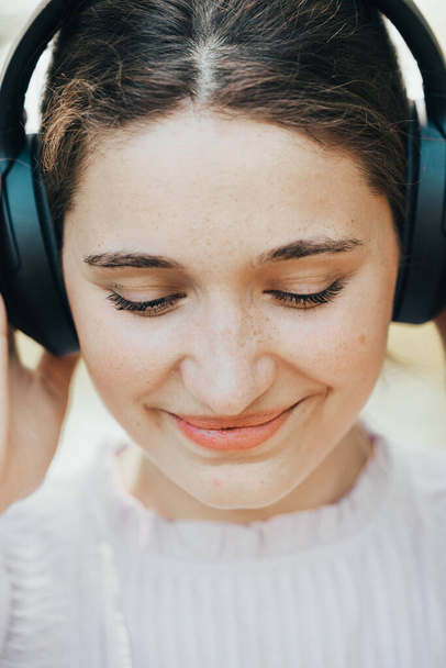 Közelről rögzítve, egy nő fejhallgatóján keresztül elmerül a zenében, a szabadság és a boldogság szimbólumaként egy szabadtéri környezetben. Ez a nyugodt zöld háttér fokozza az élményt, tökéletes - Fotó, kép
