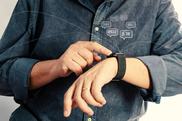 Primer plano de un hombre que interactúa con su smartwatch negro, la gestión de las notificaciones digitales, indicativo de la comunicación inalámbrica moderna. - Foto, Imagen