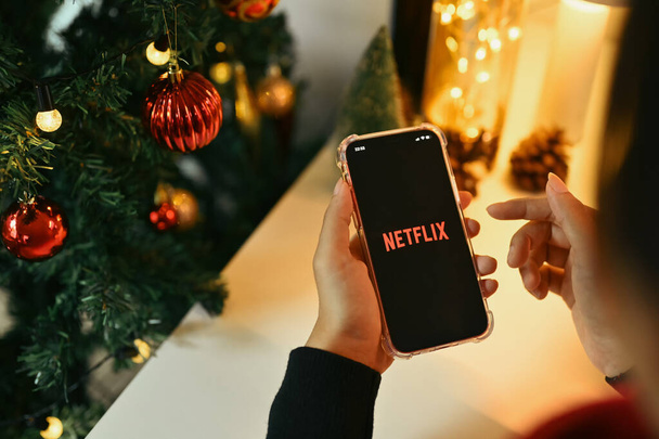 Chiang Mai, Ταϊλάνδη - Οκτ 31,2023: Γυναίκα κατέχει ένα smartphone με το λογότυπο Netflix εμφανίζεται στην οθόνη κοντά στο χριστουγεννιάτικο δέντρο. - Φωτογραφία, εικόνα