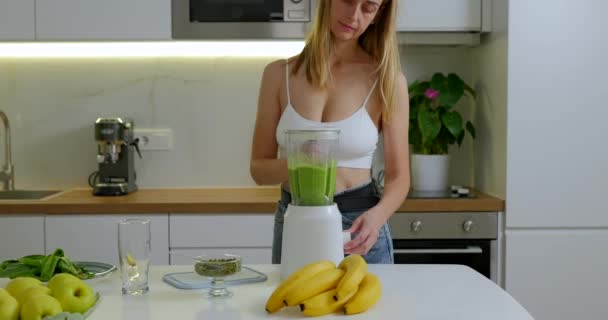Sportieve vrouw maakt groene spinazie en bananensmoothie in blender. Hoge kwaliteit 4k beeldmateriaal - Video