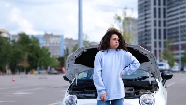 Портрет красивої молодої жінки, що стоїть на вулиці біля розбитого автомобіля, чекає на допомогу евакуатора. Жінка на вулиці біля автомобіля з відкритим капюшоном. Поломка автомобіля. Автомобільна аварія. Проблема з автомобілем
 - Кадри, відео