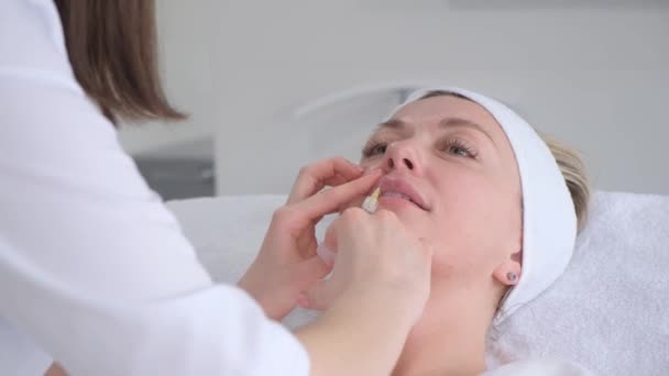 Una mujer hermosa recibe inyecciones en los labios de un médico profesional. Aumento de labios. Procedimientos cosméticos. - Metraje, vídeo