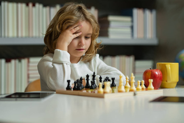 Dzieciak myśli o szachach. Dzieciak gra w szachy w szkole. Chłopiec bawi się w grę planszową. Myśląc burza mózgów dziecka i pomysł w grze w szachy. Dzieciaki wcześnie się rozwijają. Chłopak gra w szachy w domu. - Zdjęcie, obraz