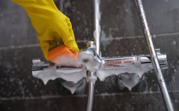 Schoonmaakster in rubber handschoen wast kraan in badkamer met spons met schuim closeup. Begrip schoonmaakbedrijf - Foto, afbeelding