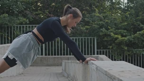 Volledig lichaam shot van Kaukasische jonge fit vrouw doen stretching oefeningen buiten overdag - Video