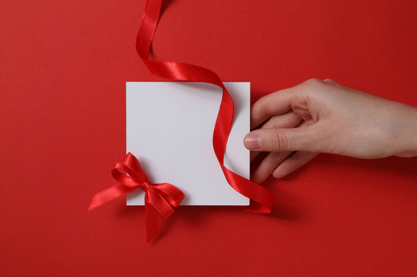 Schleifen mit Schleife und Papier in weiblicher Hand auf rotem Hintergrund, Platz für Text - Foto, Bild