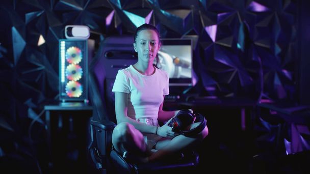 Gamer sitzt auf dem Stuhl im Gaming Club und setzt ihre Kopfhörer auf - Lutscher lutschen und in die Kamera schauen, Portrait - Foto, Bild