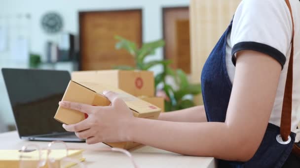 小さなスタートアップ、中小企業の所有者、アジアの女性起業家の肖像は、顧客とインナーボックスに製品を梱包する前に製品を手配するために注文を確認します。フリーランスの概念 - 映像、動画