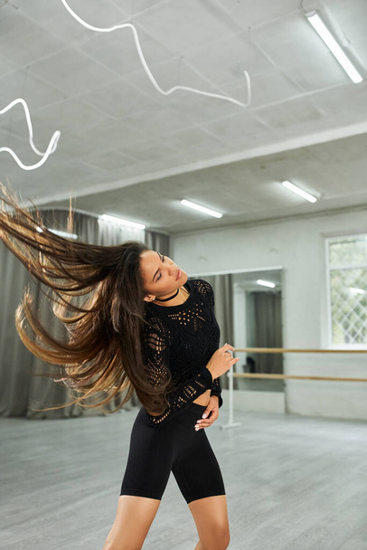 donna afro-americana dai capelli lunghi in abito nero che prova la danza ritmica nella sala moderna - Foto, immagini