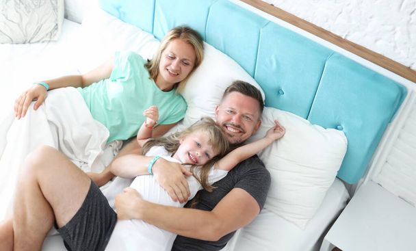 Mladý muž a žena leží s malou holčičkou v posteli. Koncept dovolené s dětmi - Fotografie, Obrázek
