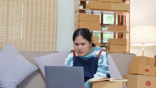 独立系アジア人女性起業家の小さな起業家は、オンラインマーケティングパッケージボックスアイテムと中小企業の配信コンセプトの陽気な成功とコンピュータのラップトップを使用して笑顔。高品質4k - 映像、動画
