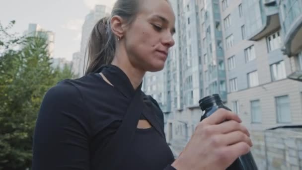 Κλίση του αθλητισμού νεαρή Καυκάσια γυναίκα πόσιμο νερό μετά την άσκηση σε εξωτερικούς χώρους το πρωί - Πλάνα, βίντεο