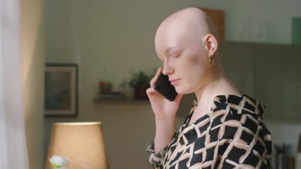 Mittlere Nahaufnahme eines positiven jungen glatzköpfigen Mädchens, das mit ihrem Freund telefoniert, während sie Zeit allein drinnen verbringt - Filmmaterial, Video