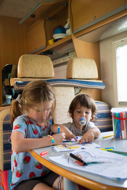 Deux enfants caucasiens, frère et sœur, dessinant sur un camping-car lors d'un arrêt sur la route. Vacances en camping-car avec enfants. Plan vertical. - Photo, image