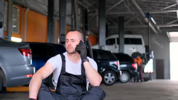 A car mechanic is talking on the phone in a car workshop. - Footage, Video