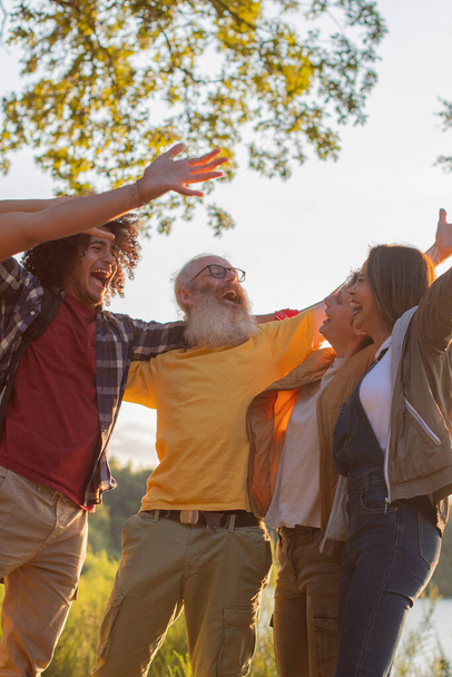 eri-ikäiset ystävät halaavat yhdessä luonnossa auringonlaskun taustalla juhlimassa hyvää kävelyä yhdessä luonnossa, tuhatvuotiset ihmiset nauravat, korkealaatuinen valokuva - Valokuva, kuva