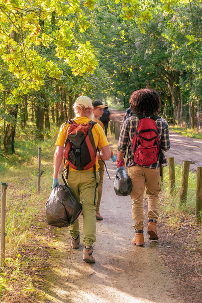 groep vrijwilligers toeristen gekleed in comfortabele wandelkleding lopen samen in het bos om afval te verzamelen, het dragen van zwaarden en handschoenen, het concept van ecologie en reinheid, Hoge kwaliteit foto - Foto, afbeelding