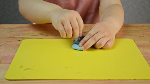 The child kneads the plasticine with his hands and cuts it with a plastic knife. Development of children's motor skills. Distance learning at home. - Footage, Video