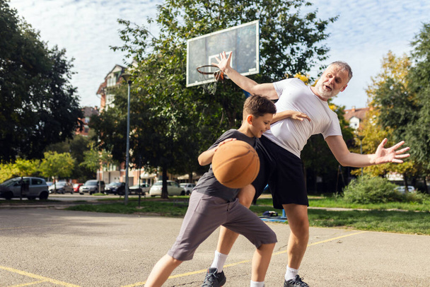 Зрелый мужчина играет в баскетбол со своим сыном - Фото, изображение