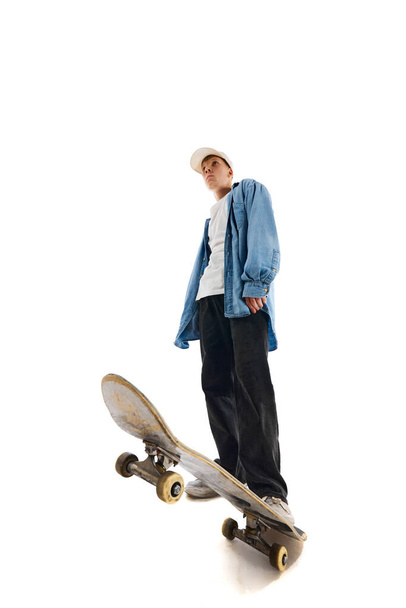 Bottom view image of teen boy in casual clothes standing with skateboard isolated over white background. Concept of professional sport, competition, training, action. Copy space for ad - Fotó, kép
