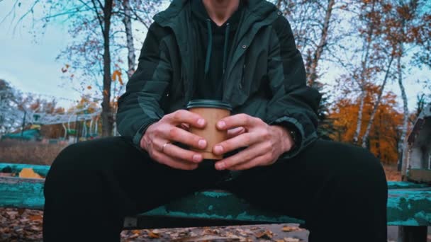 Miehen kädet ottavat lasin kahvia lähikuva syksyllä ilmapiirissä. Nuori mies juo kahvia kävellessään puistossa. Elämäntapa. Syksyn kävelee käsite. - Materiaali, video