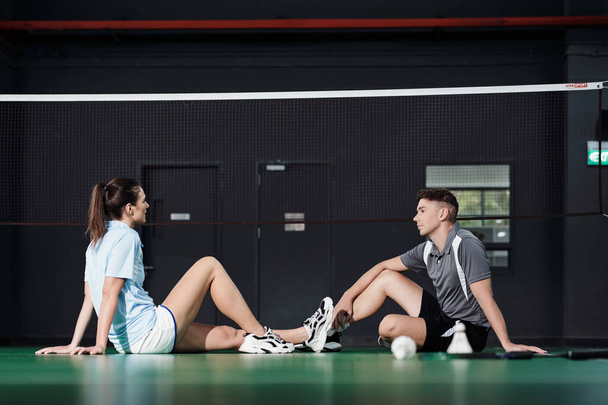 Giovane coppia seduta sul pavimento a rete e discutere gioco di badminton - Foto, immagini