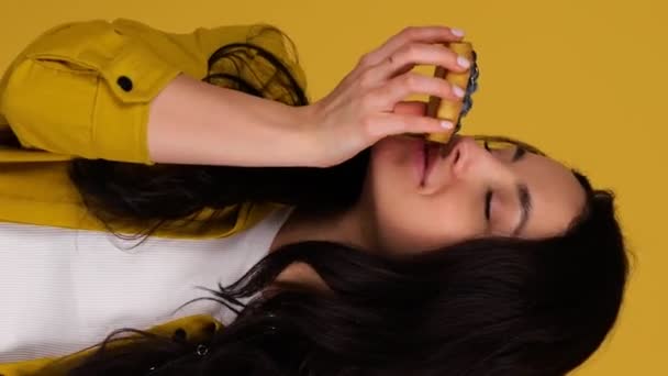 Sorrindo linda senhora posando no estúdio enquanto segurava duas tartes de mirtilo. Isolado em fundo amarelo. Comida, conceito de estilo de vida. Vídeo vertical em tempo real - Filmagem, Vídeo
