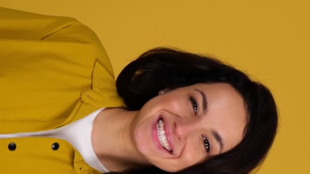 Donna attraente sorridente che tiene e vomita un'arancia, posando sullo sfondo giallo. Concetto nutrizionale sano. Video verticale in tempo reale - Filmati, video
