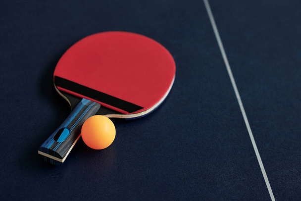 Червоний настільний теніс ракетка і помаранчева куля на столі, вибірковий фокус - Фото, зображення