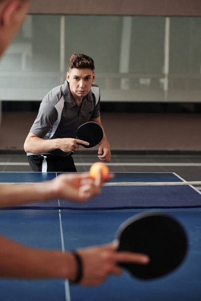 Серйозний молодий чоловік грає в настільний теніс з другом у спортзалі під час тренування для змагань - Фото, зображення