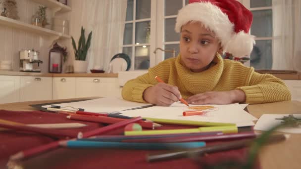 Pugnalata di bella ragazza afroamericana di 6 anni seduta al tavolo della cucina e che disegna foto durante le vacanze di Natale - Filmati, video