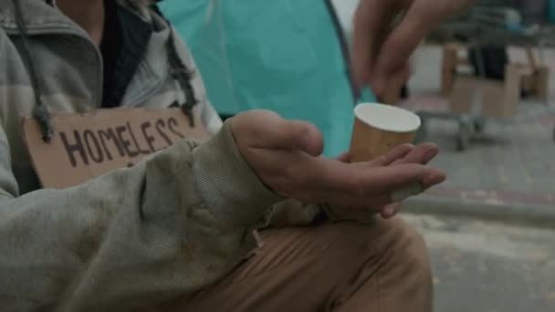 Gehakt schot van zwerver in vuile kleren met beker nemen van geld van onbekende persoon, zitten naast tent - Video