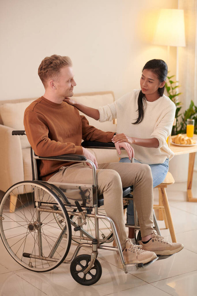 Заботливая девушка поддерживает молодого человека, приспосабливающегося к жизни в инвалидном кресле после автомобильной аварии - Фото, изображение