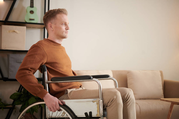 Jovem sério com deficiência movendo-se em casa em cadeira de rodas - Foto, Imagem