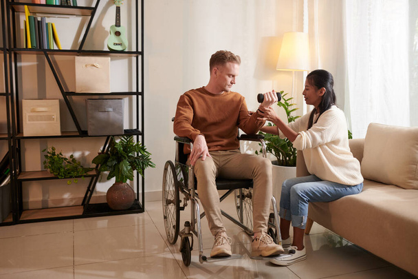 Φροντιστής εξηγώντας ασθενή σε αναπηρική καρέκλα πώς να κάνει άσκηση με αλτήρες - Φωτογραφία, εικόνα