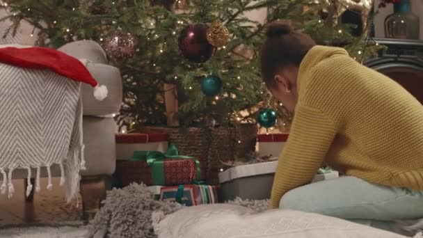 Vzrušený Afroameričan 6 letá dívka otevírá vánoční dárky ležící pod borovicí v krabicích v teplém útulném bytě na Štědrý den - Záběry, video
