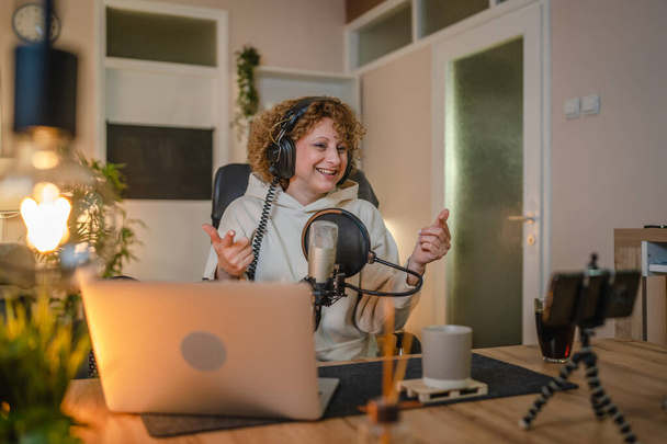 Одна жінка кавказька жінка-блогер або відеоблогер жартівливий під час потокового відео подкасту в студії мовлення використовує мікрофон та навушники відомий впливовий знімок відео для подкасту каналу
 - Фото, зображення