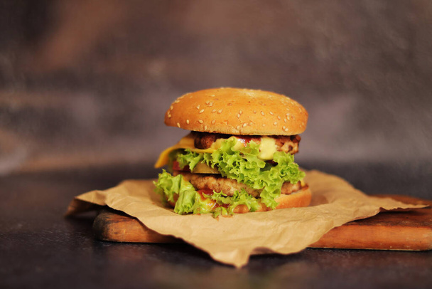 Doppelter Cheeseburger auf grauem Hintergrund. Saftiger leckerer Burger auf Bastelpapier, Seitenansicht. Fast food. Kopierraum - Foto, Bild