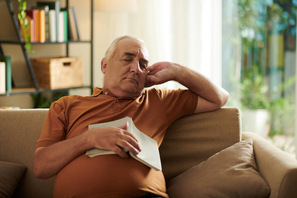 Starší muž usnul na gauči v obývacím pokoji při čtení románu - Fotografie, Obrázek