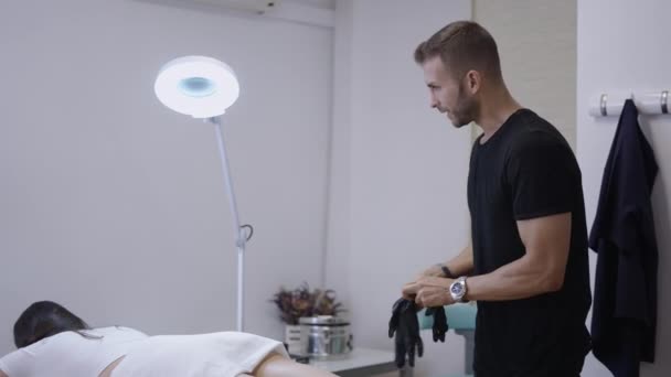 Kaukasische mannelijke verpleegkundige dons handschoenen mesotherapie uit te voeren op de patiënt - 4K Healthcare - Video