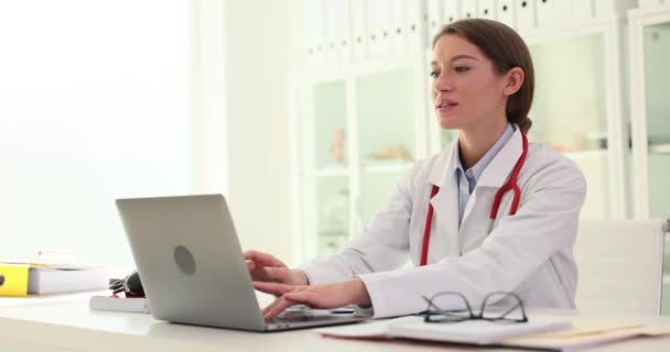 Kadın doktor dizüstü bilgisayarda çalışıyor ve klavyede daktilo kullanıyor. Tıp işçilerinin çalışma günü bitti. - Video, Çekim